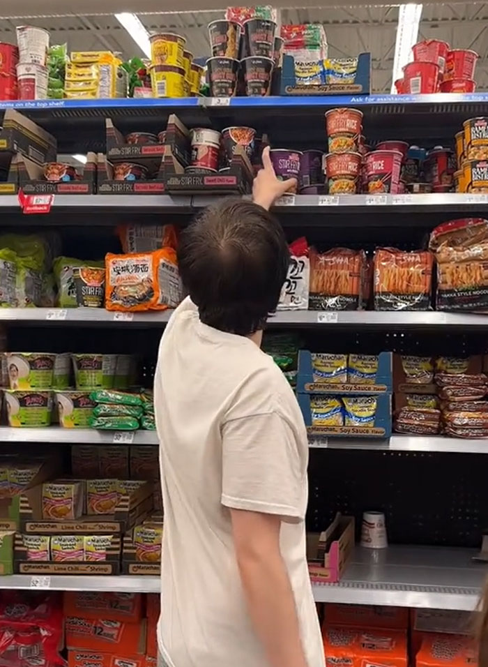 American parents fill the whole cart of groceries. A person reaching for instant noodles on a supermarket shelf. American parents fill the whole cart of groceries. A person reaching for instant noodles on a supermarket shelf.