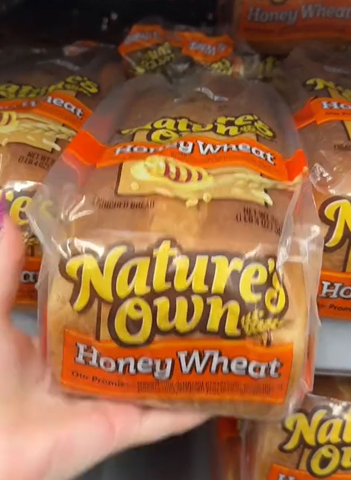American parents shopping for groceries; hand reaching for a loaf of Nature's Own Honey Wheat bread on a grocery store shelf. American parents shopping for groceries; hand reaching for a loaf of Nature's Own Honey Wheat bread on a grocery store shelf.