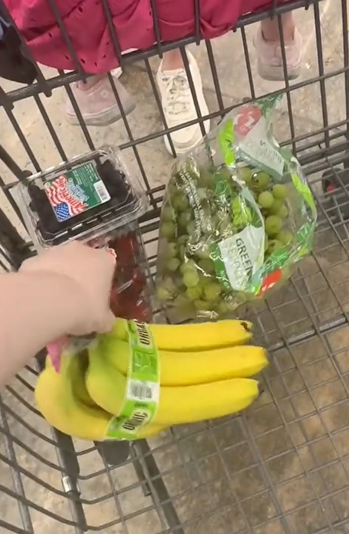 American parents grocery cart: a hand placing bananas into a grocery cart already containing grapes, strawberries, and blueberries. American parents grocery cart: a hand placing bananas into a grocery cart already containing grapes, strawberries, and blueberries.