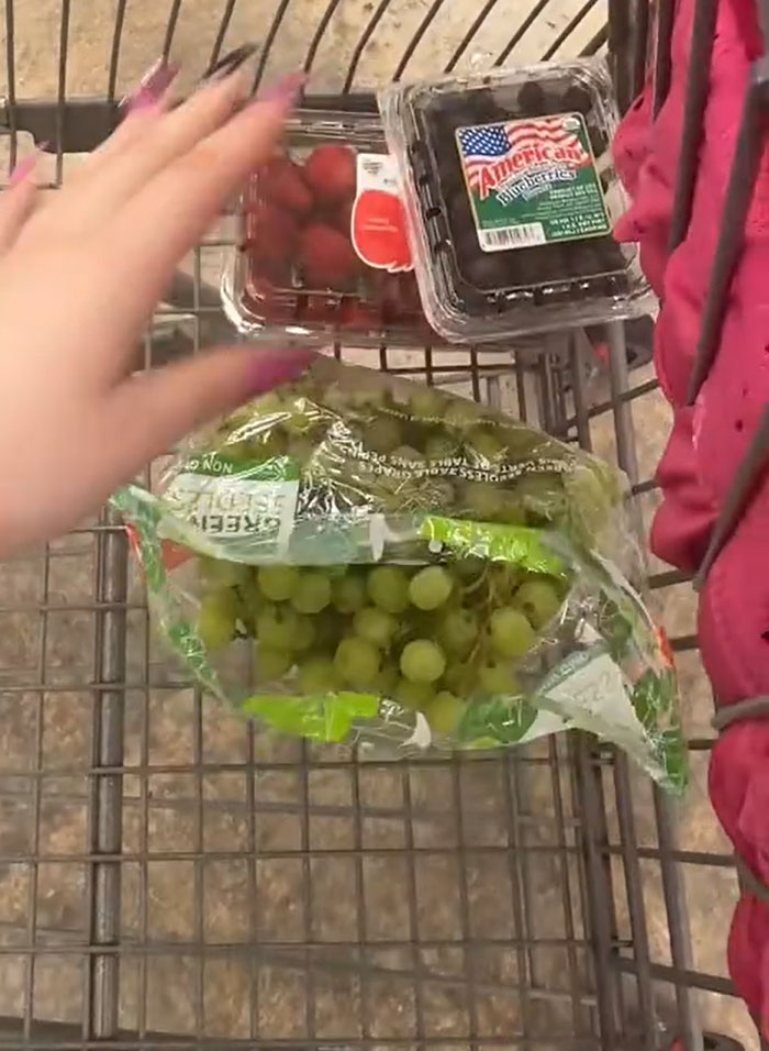 American parents grocery cart: a hand reaching for a container of strawberries in a grocery cart with grapes and blueberries. American parents grocery cart: a hand reaching for a container of strawberries in a grocery cart with grapes and blueberries.