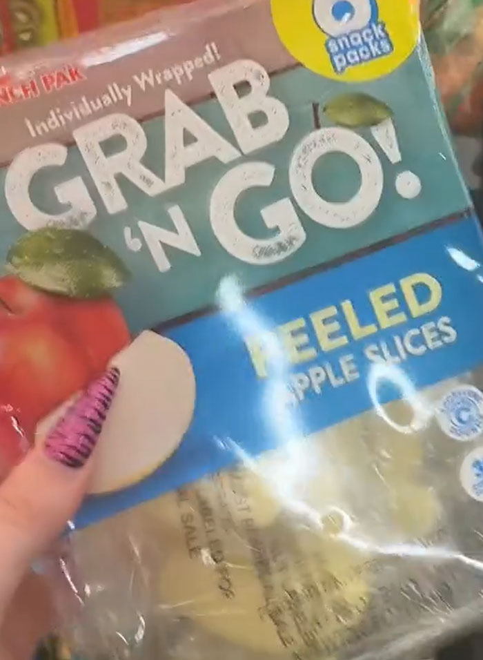 American parents fill cart with groceries: a hand holding a bag of Grab 'n Go peeled apple slices. American parents fill cart with groceries: a hand holding a bag of Grab 'n Go peeled apple slices.