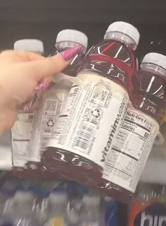 A hand reaches for a pack of Vitamin Water, American parents fill grocery cart with groceries. A hand reaches for a pack of Vitamin Water, American parents fill grocery cart with groceries.