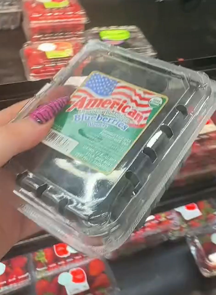 Hand holding a container of American blueberries in a grocery store, part of a full cart of groceries for American parents. Hand holding a container of American blueberries in a grocery store, part of a full cart of groceries for American parents.