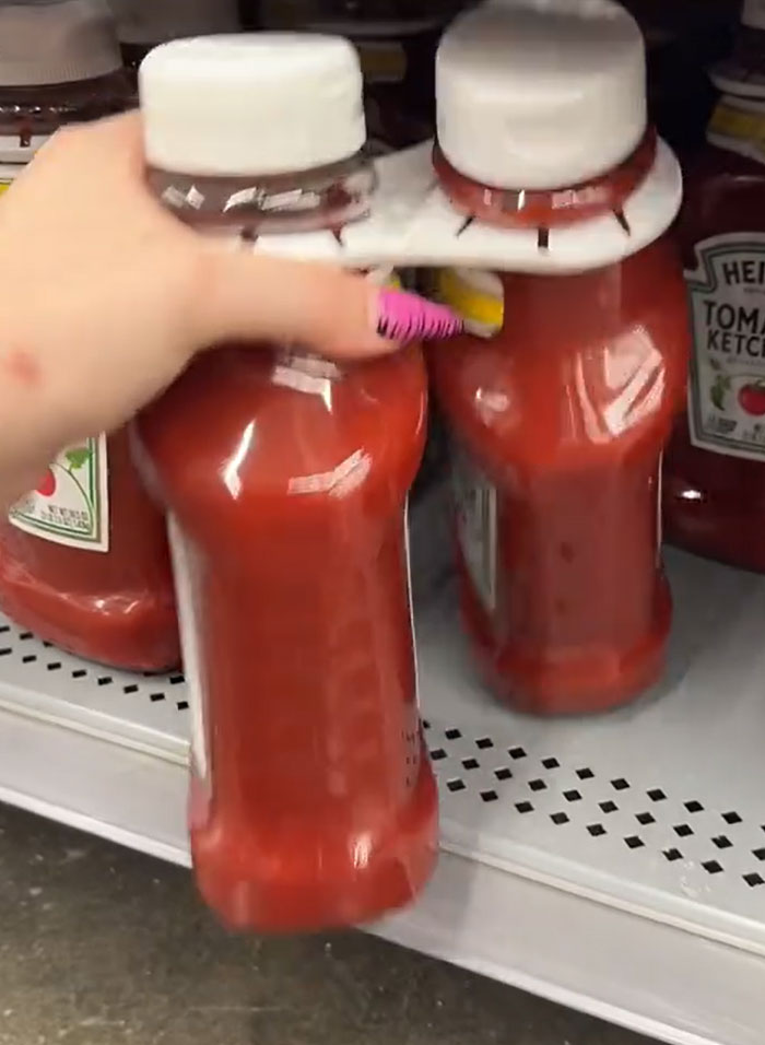 A hand holding two bottles of ketchup in a grocery store aisle. Parents buying groceries. A hand holding two bottles of ketchup in a grocery store aisle. Parents buying groceries.