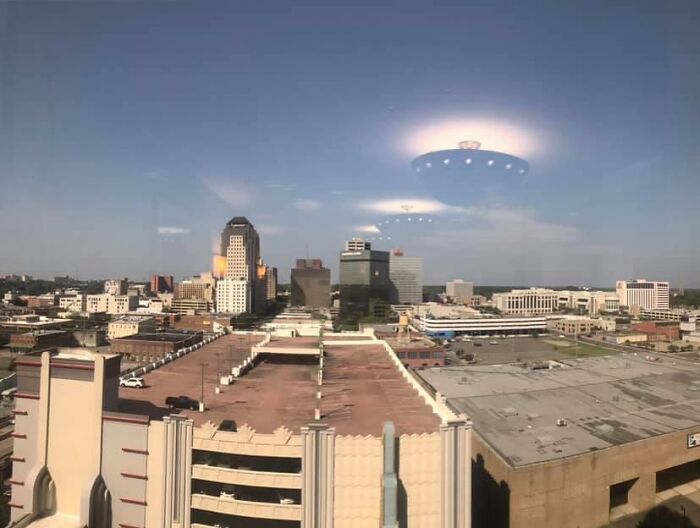 UFO-like reflection of a ceiling lamp on a window overlooking a city skyline.
