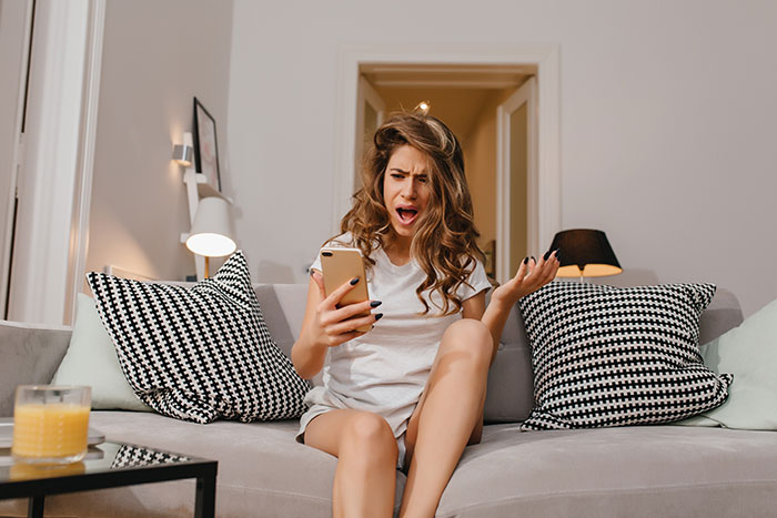A woman looking shocked while checking her phone, discovering the MOH made guests pay for the bridal shower.