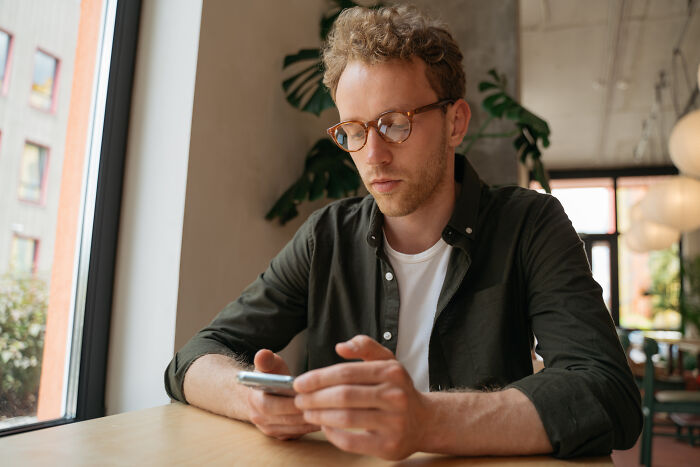 A man in glasses looking at his smartphone, reflecting on satisfying stories