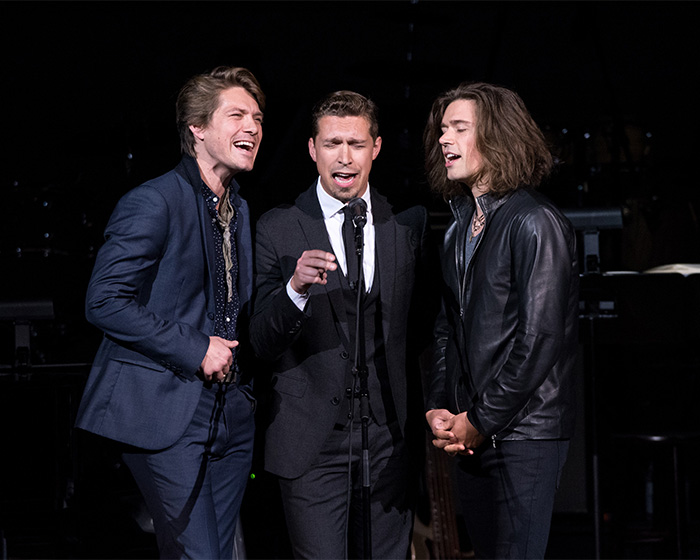 Hanson brothers singing together on stage in formal and leather outfits