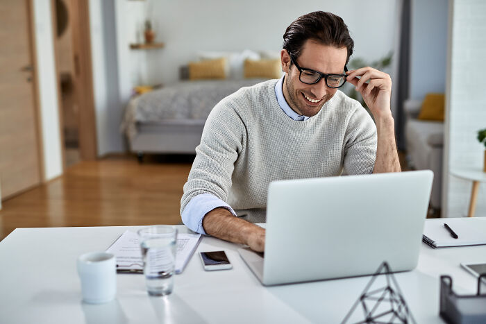 A smiling man wearing glasses and working on a laptop, perfect for satisfying stories