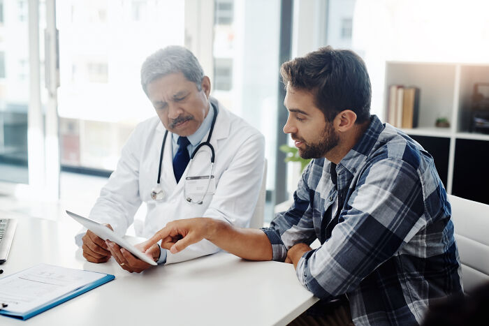 A doctor consults with a male patient, discussing his pain reactions to medical conditions.