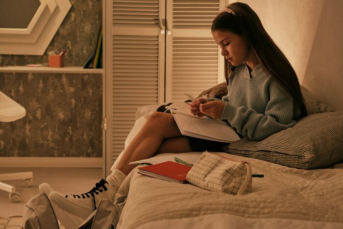 A child studying on a bed, a kid navigating life, potentially facing challenges with parents not letting them live freely.