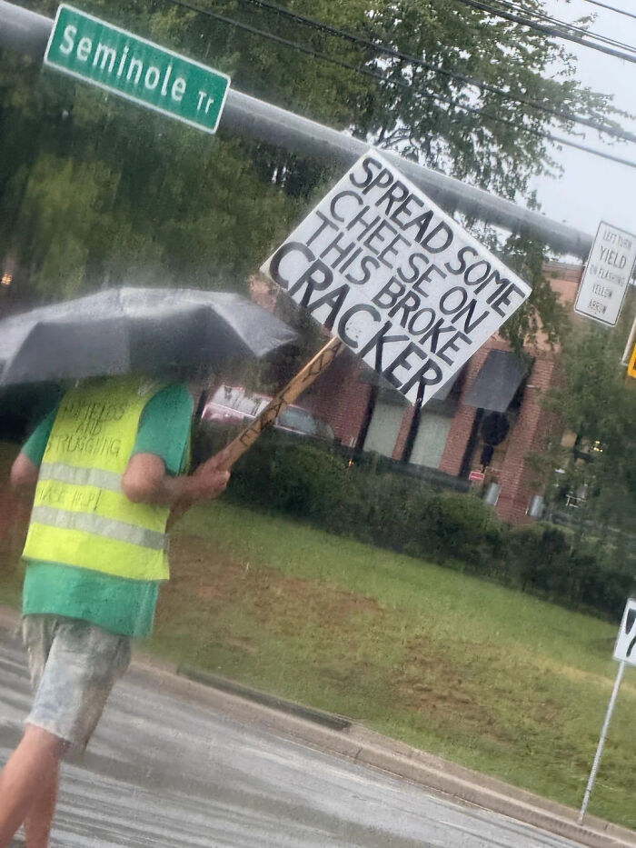 Hilarious photos: A person holding an umbrella and a sign that reads Spread Some Cheese On This Broke Cracker in the rain.