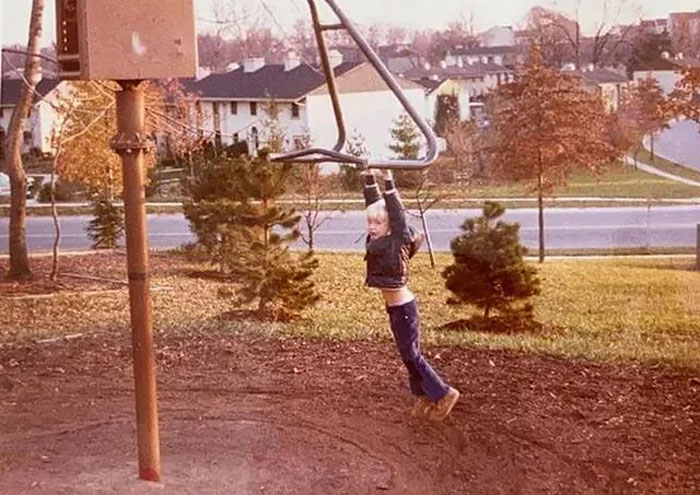 A young boy hanging from a metal bar on a playground, with no safe landing area below, a true playground fail.