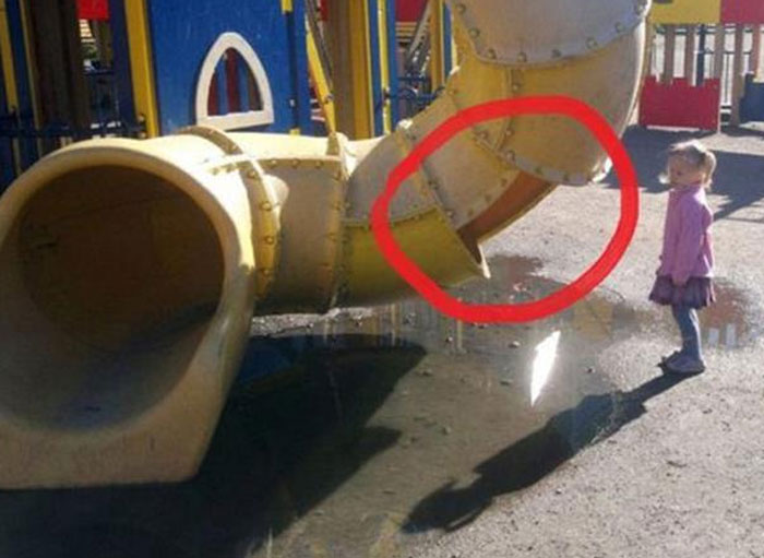 A little girl standing by a playground slide that ends abruptly, highlighting a dangerous playground fail.