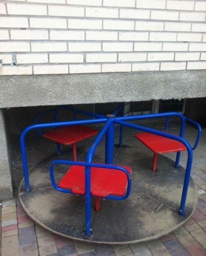 A poorly designed playground merry-go-round partially hidden under a brick wall, showcasing a playground fail.