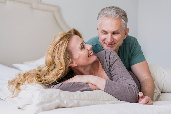 A happy couple smiling in bed, representing a husband and wife discussing a vasectomy and insurance. A happy couple smiling in bed, representing a husband and wife discussing a vasectomy and insurance.