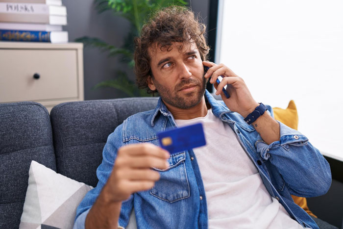 A man on the phone, holding a credit card, worried about his spending and separated finances.