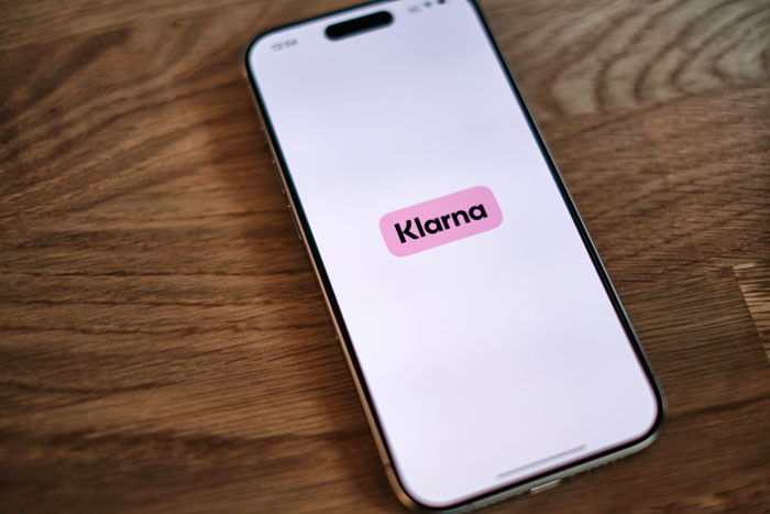 A smartphone displaying the Klarna app logo, related to the husband's spending and separate finances.