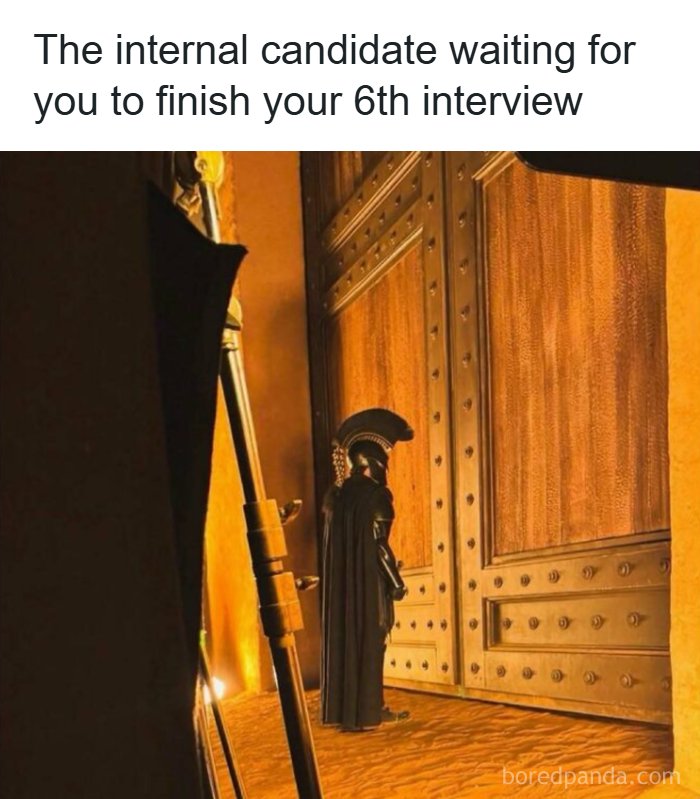 Pop culture post: A person in a black costume stands before a large golden door, like an internal candidate waiting for an interview, for good vibes.
