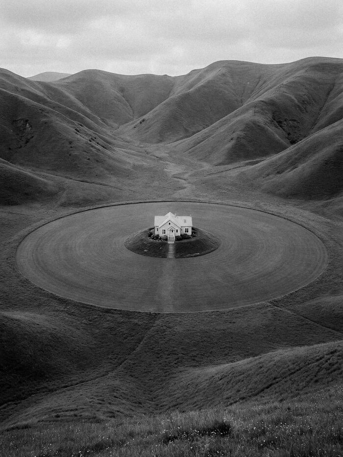 A lone house encircled by a perfect green ring in a vast, desolate valley, a surreal image of distorted reality.