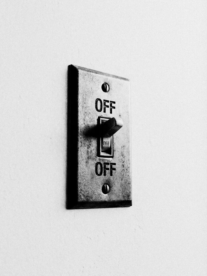 Black and white close-up of a light switch with multiple OFF labels, representing distorted reality in a surreal image.