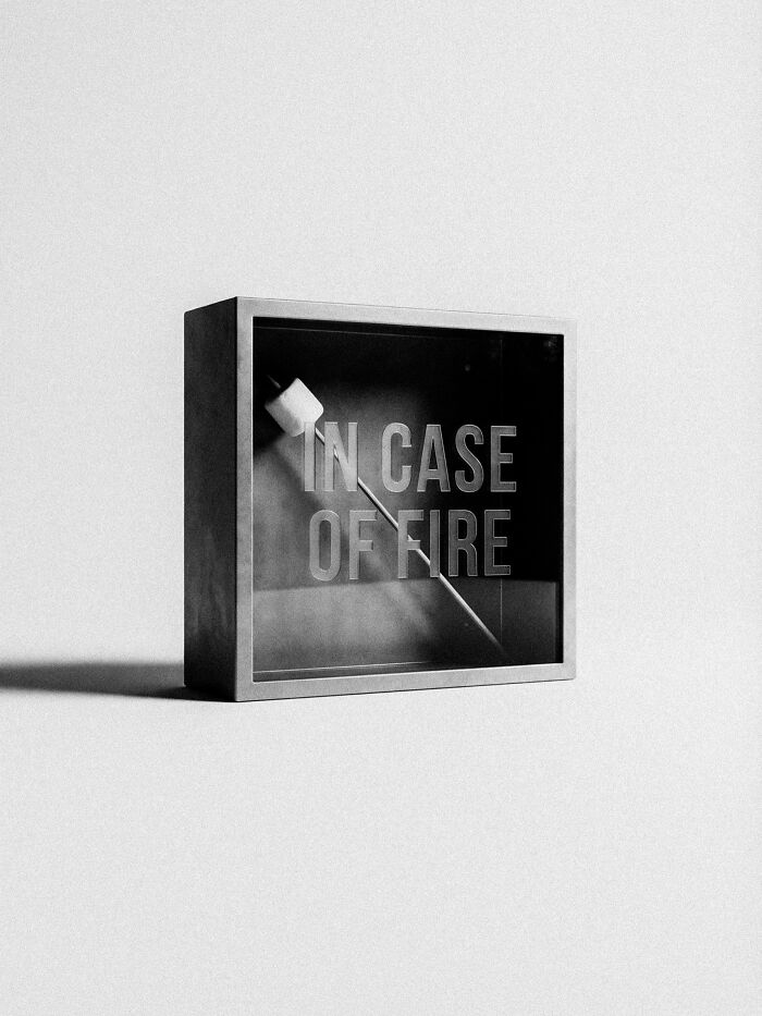 A box with a marshmallow on a stick inside, labeled IN CASE OF FIRE, a surreal and dystopian image.