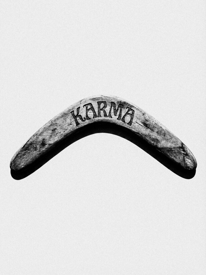 A boomerang with the word KARMA carved into it, a surreal and dystopian image.