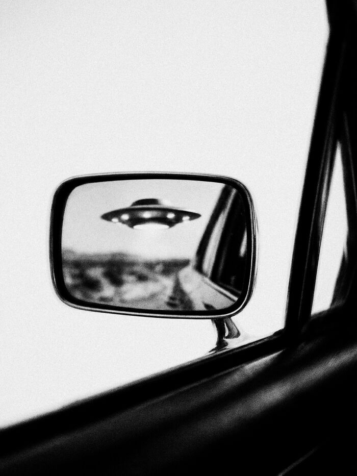 A UFO reflected in a car's side mirror, a surreal and dystopian image from Marcus Wallinder.