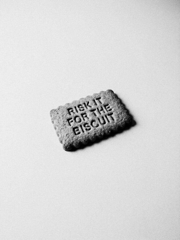 A black and white close-up of a biscuit with 'RISK IT FOR THE BISCUIT' written on it, representing surreal and dystopian imagery.