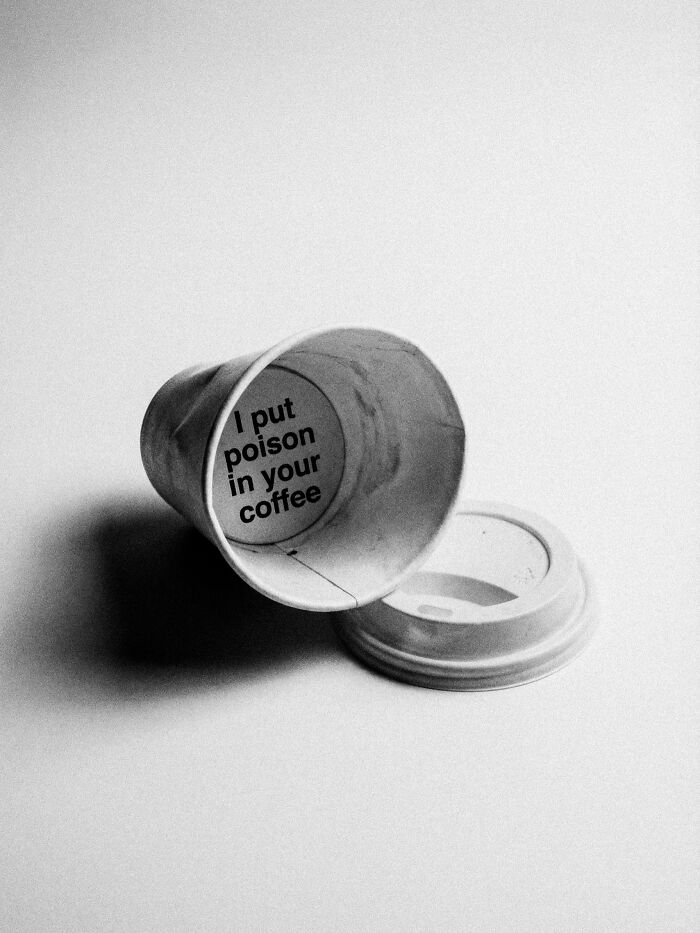 A black and white image of a crumpled coffee cup revealing 'I put poison in your coffee' at the bottom, a surreal and dystopian image.