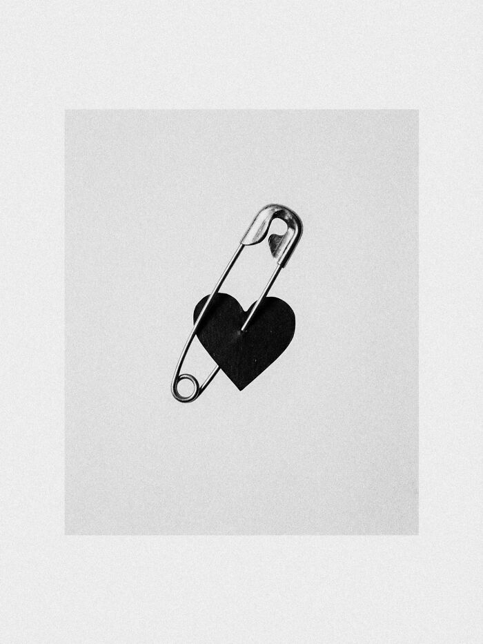 A black and white image of a safety pin piercing a small black heart, a dystopian image by Marcus Wallinder.