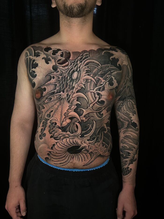 Stunning mythology tattoo of a dragon and waves covering a mans torso and arm, from Sacred Gold Studio.