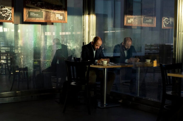 A street photographer captures an odd coincidence: a man reflected in a window, appearing to be two people in a cafe.