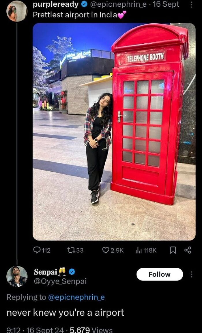 Woman leaning on large red telephone booth at airport, called prettiest airport in India
