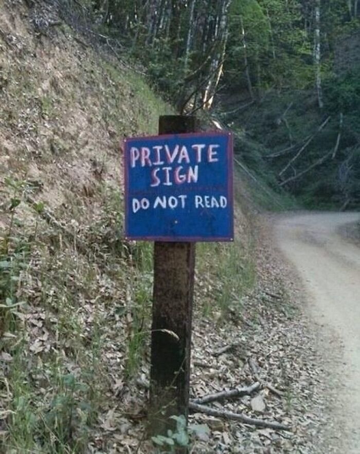 A funny sign post in a forest reads PRIVATE SIGN DO NOT READ, creating a paradox.
