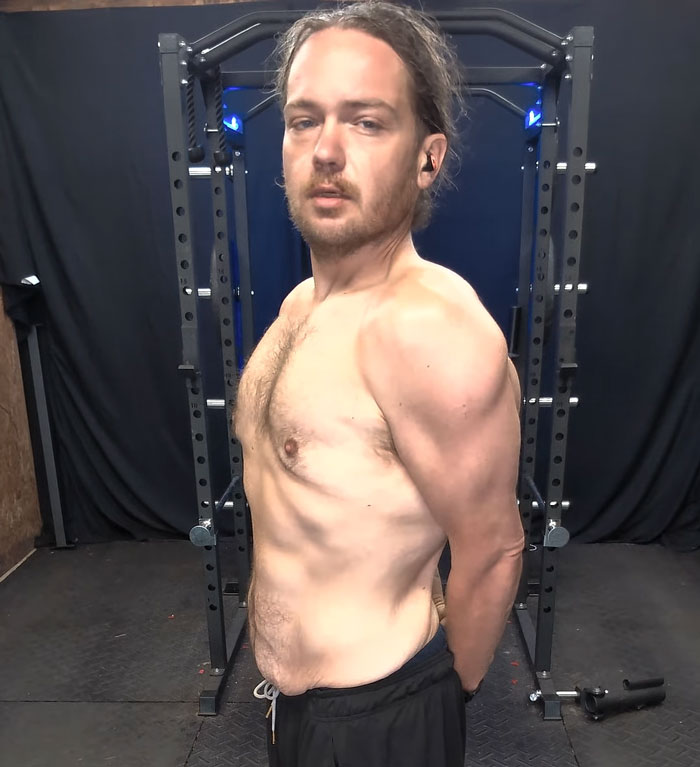 A man shows his incredible weight loss transformation, posing shirtless in a gym with a power rack behind him. A man shows his incredible weight loss transformation, posing shirtless in a gym with a power rack behind him.