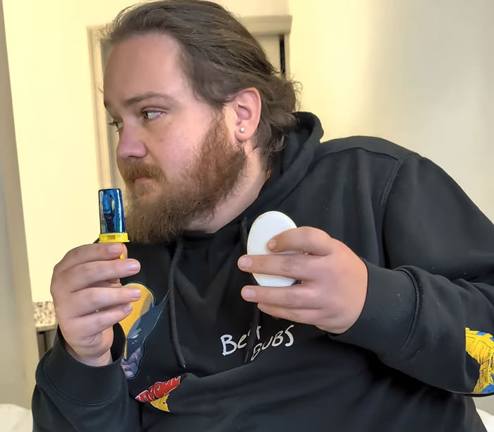 A man with a beard holds an inhaler and a white oval object. Focus on his serious expression during his weight loss transformation. A man with a beard holds an inhaler and a white oval object. Focus on his serious expression during his weight loss transformation.