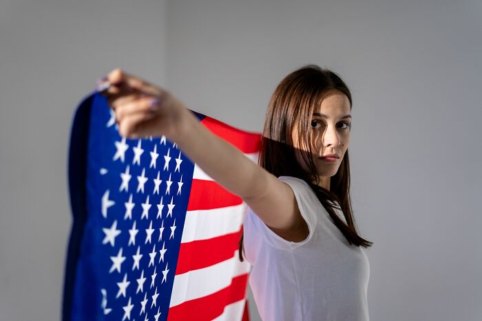 A serious woman holding an American flag over her shoulder, reflecting industries that are about to collapse.