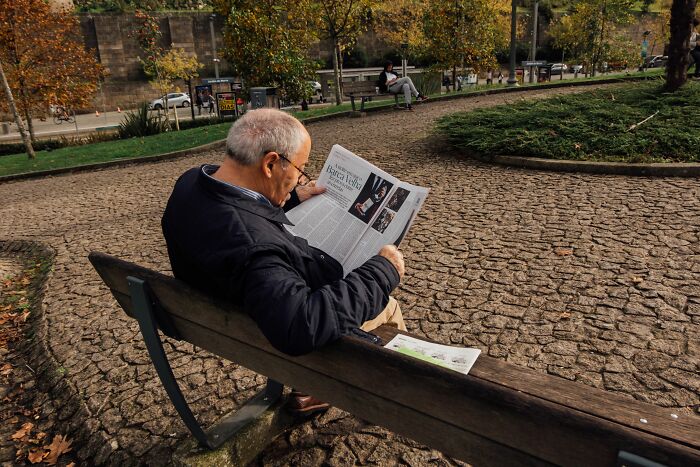Elderly man reading a newspaper on a park bench, showing an industry about to collapse.