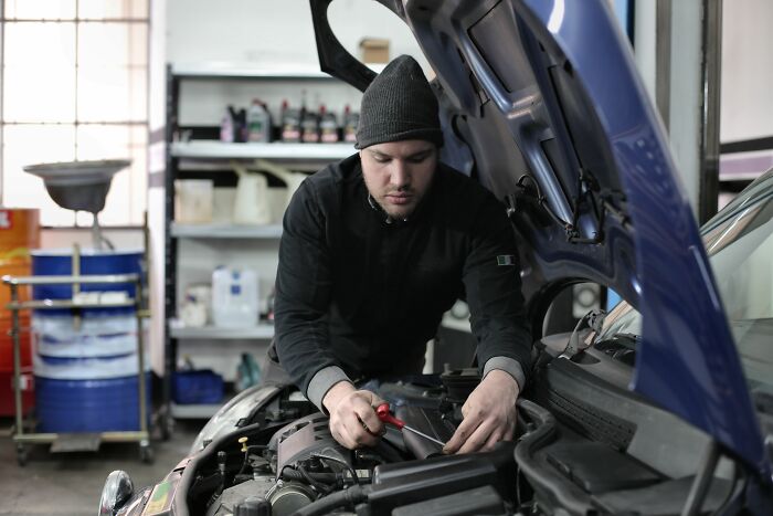 A mechanic in a beanie works on a car engine in a garage, symbolizing industries that are about to collapse.