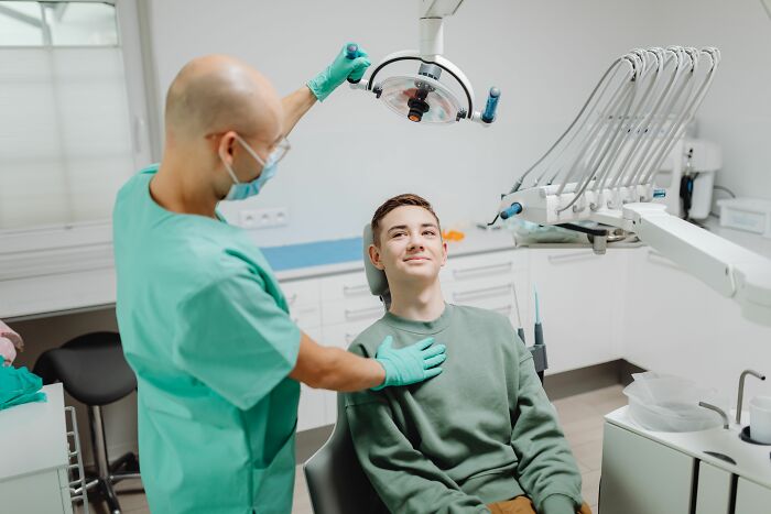 A dentist with a mask and gloves adjusts a light over a smiling patient, representing industries that are about to collapse.