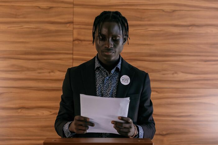 A person in a suit with a VOTE button on their lapel, reading a document, representing industries collapsing.