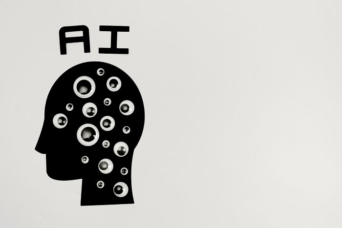 A black cutout of a human head with circles inside, topped by the letters AI, symbolizing industries collapsing due to AI.