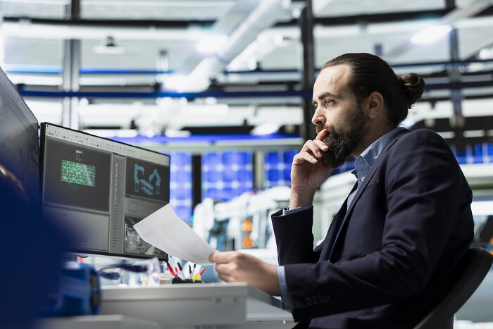 A focused engineer examines data on a computer in a modern office, depicting industries about to collapse due to tech shifts.