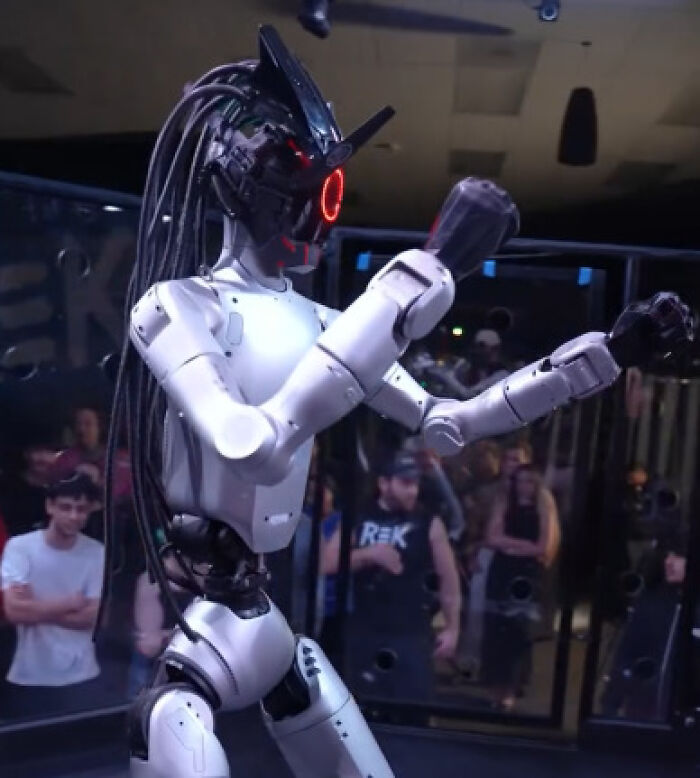 Futuristic robot with red glowing eyes and braided cables ready to fight in cage