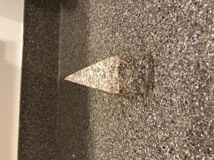 A triangular granite shelf perfectly synced in texture and color with a speckled gray wall.