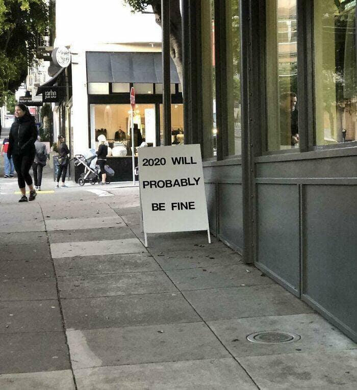 A sidewalk sign reads 2020 WILL PROBABLY BE FINE, an example of beliefs and words that age badly.