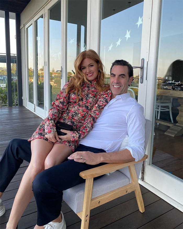 Isla Fisher and her ex-husband, after her divorce, sitting together on a balcony, smiling.