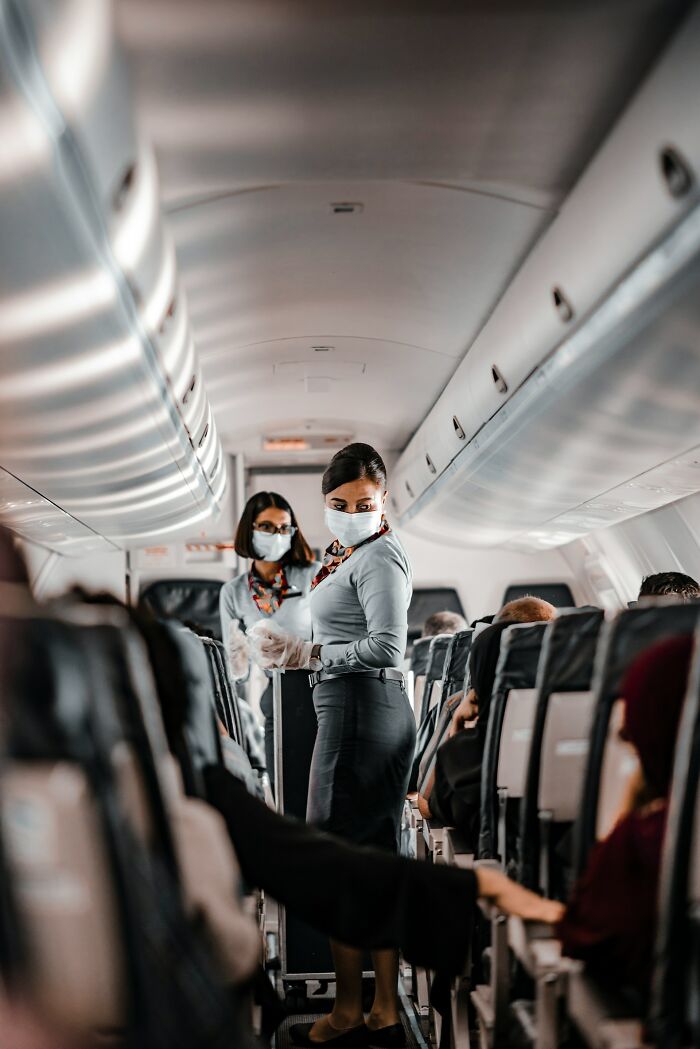 Two masked cabin crew members stand in an airplane aisle, demonstrating things cabin crew deal with.