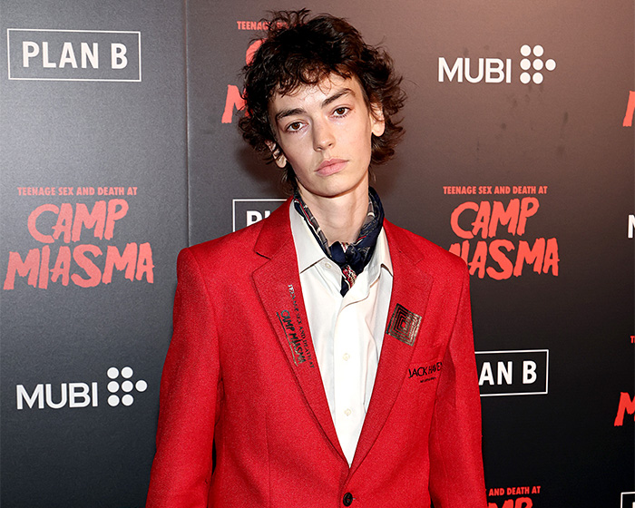 Trans actor Jack Haven poses on a red carpet wearing a striking red blazer and neck scarf Trans actor Jack Haven poses on a red carpet wearing a striking red blazer and neck scarf